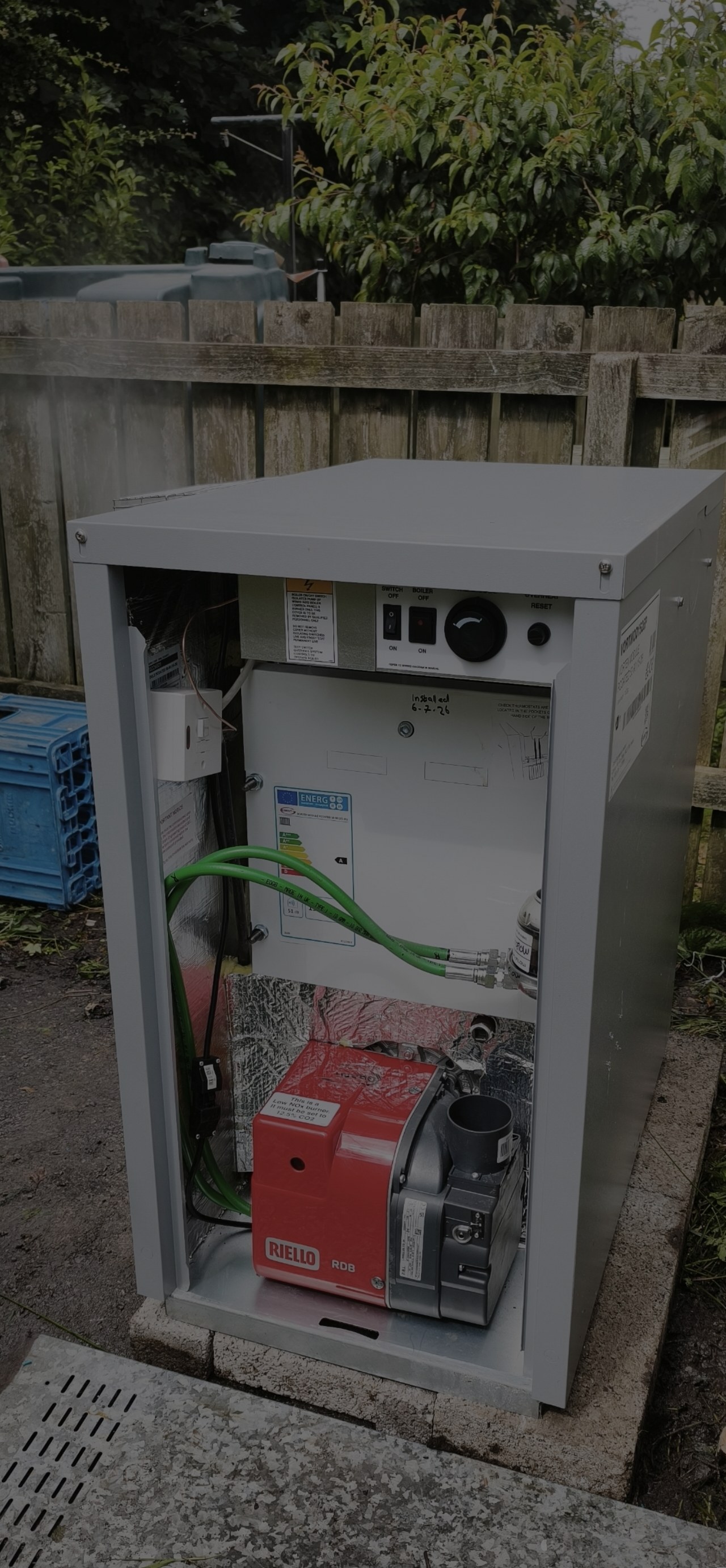 Grey external oil boiler housing with the front off, showing the controls and a red burner inside