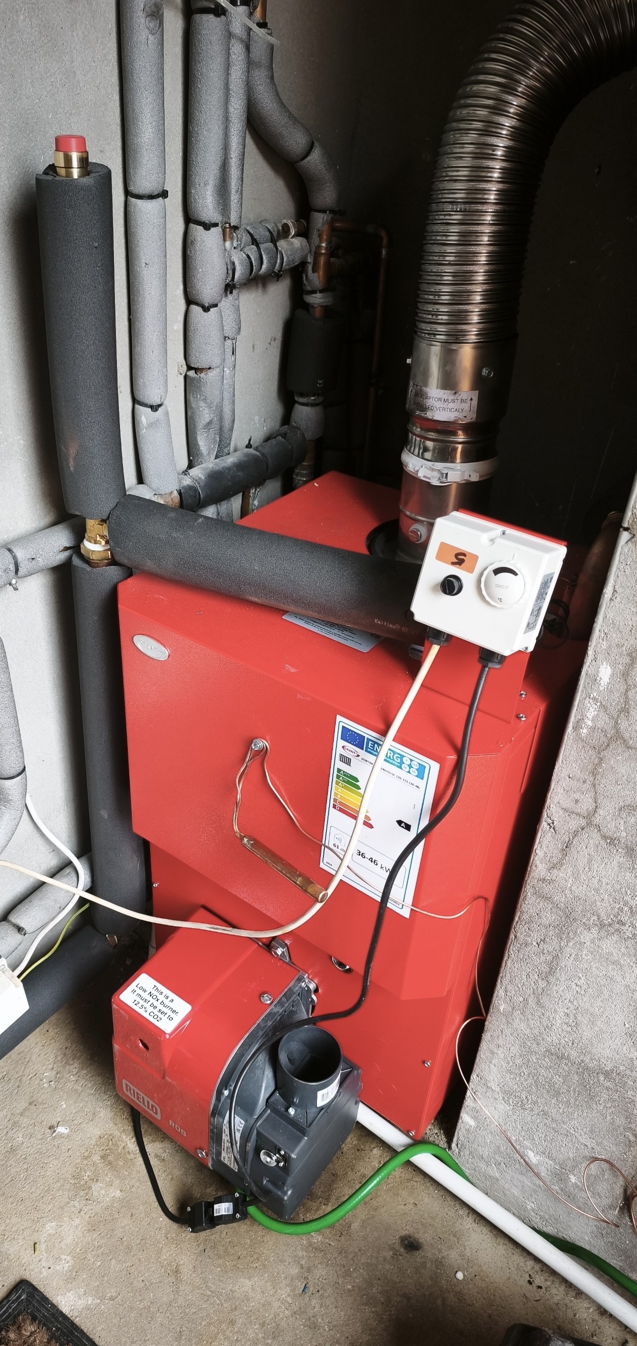 Red oil boiler and burner in a utility space, with a flexible flue liner and insulated pipes above