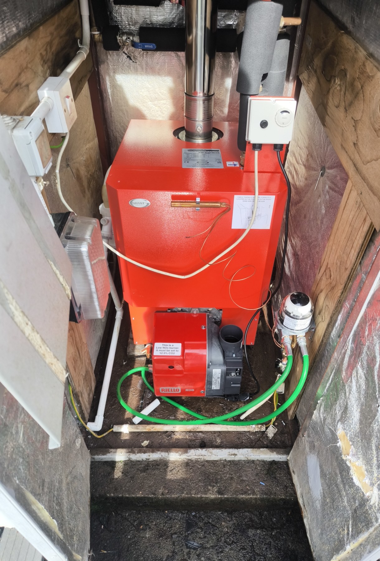 Red oil boiler with its burner and green oil line in a narrow boiler house, seen from above